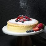 Aamna Junaid - Sponge cake dusted with sugar and topped with berries against a black background.