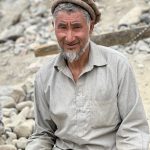 Aamna Junaid - An older man with grey beard and shirt sitting in front of a pile of rubble.