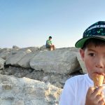 Alex Wong - A young boy eats an ice cream in front of a rocky outcrop with another child sat on the rocks behind.