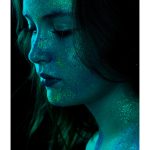 Ella Martin - Portrait of a young woman in blue glittery light against a black backdrop.