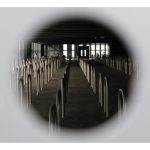 Elliott Hilsden - View through a hole into a room full of empty bike racks, vignetted by white.