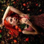 Isabella Wilson - Portrait image of a girl in a red wig and dress, laying on a bed of roses.
