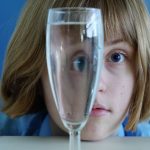 Joshua Kiddell - A young girl with a brown bob looks through a champagne glass full of water.