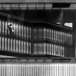 Polly Simpson - Black and white image of a person walking down a double flight of concrete stairs.