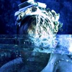 Oana Gabriela Babenco - Fantasy like image. Portrait of a person behind a plastic/glass container with water in. They look wet and are wearing a headdress. The main colour of the photo is blue.