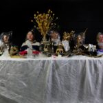 Sonnie Winter - Table with seven people sitting at it with plastic bags on their heads, the table is scattered with objects like bones, birds wings, taxidermy and fruit