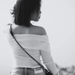 Vy Dinh - Black and white photograph of a lady looking over her shoulder, her back is facing us. They are wearing an off the shoulder top and jeans